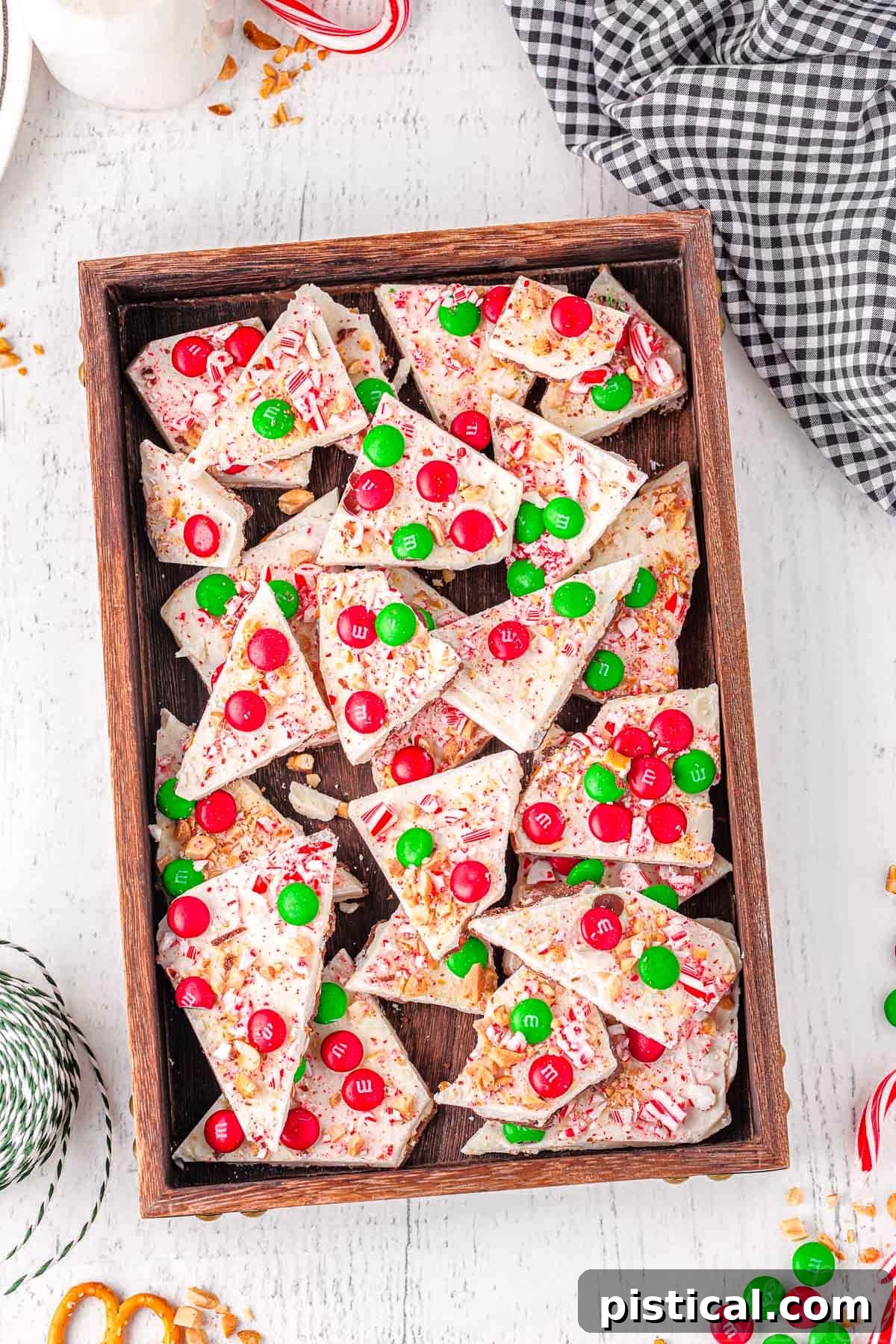 top down look at a lot of christmas decorated chocolate bark in a dark wooden tray.