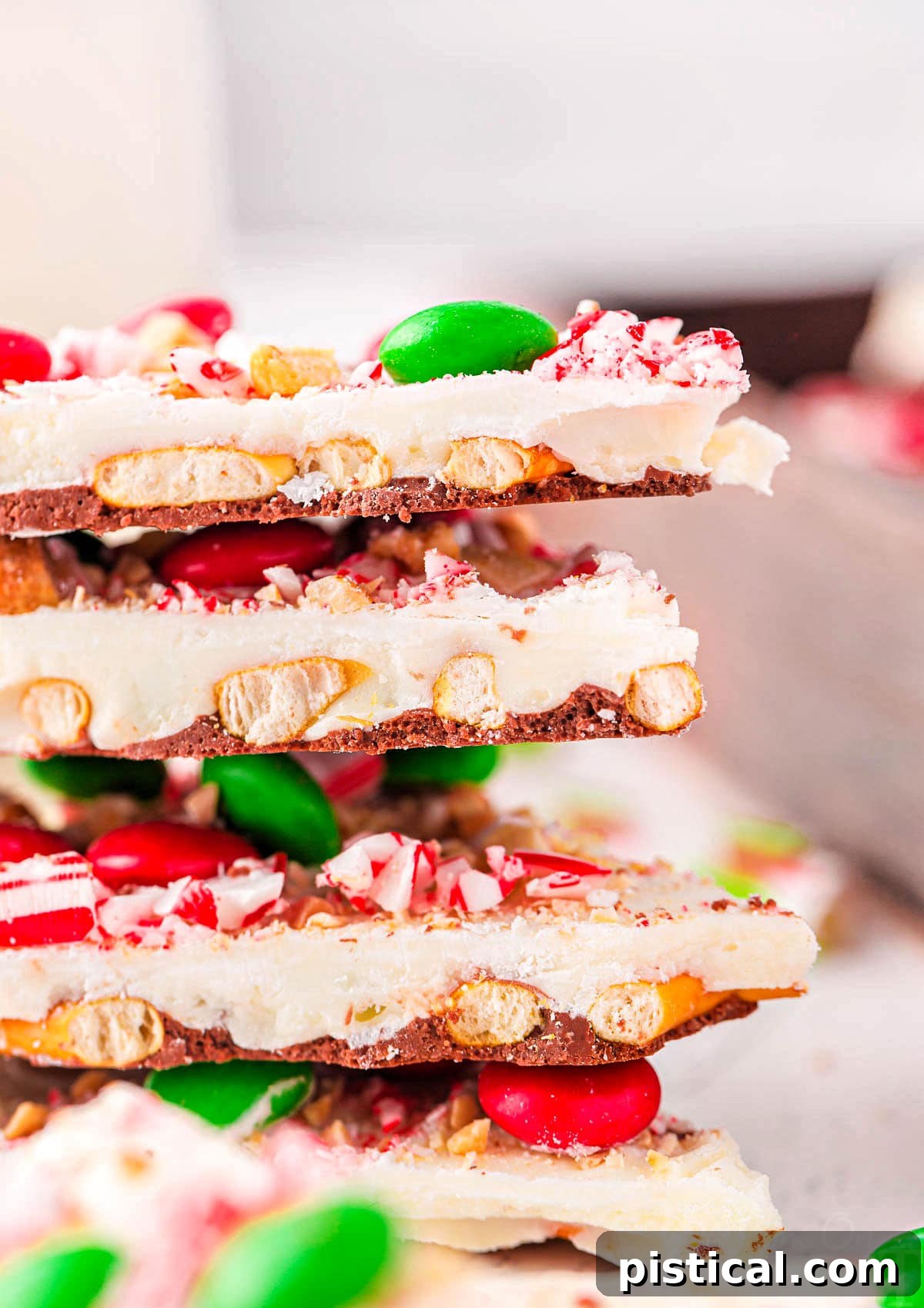four pieces of christmas bark stacked on top of each other. the bark is made with pretzels, m and ms, and candy canes.