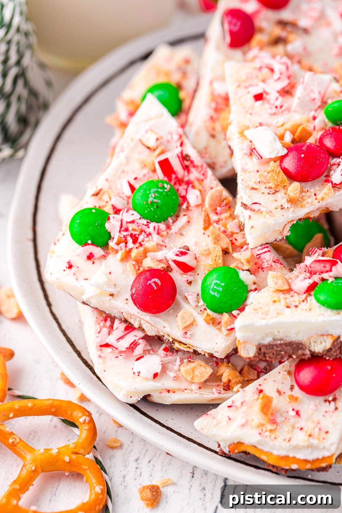 christmas candy bark on a white plate. the bark is decorated with christmas candy and made with pretzels.