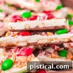 top down look at pieces of chocolate bark layered in a shallow wood tray. bark is decorated for christmas.