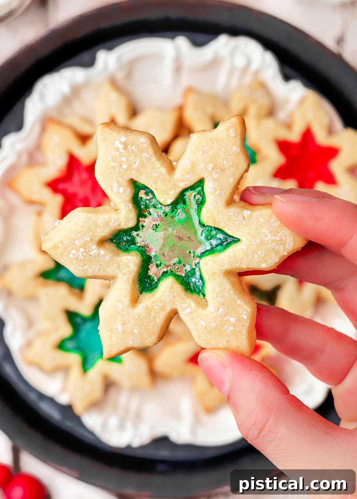 Crystal Window Bites 2 hand holding stained glass cookie over a plate of more cookies. centers are green and red.