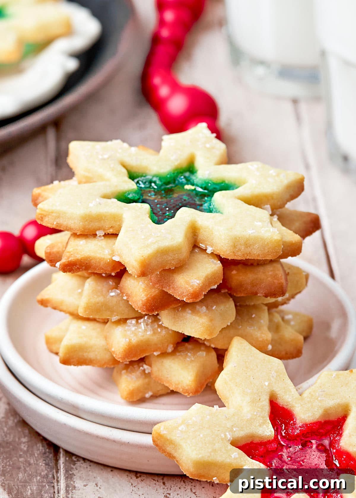 Crystal Window Bites 7 stack of stained glass cookies on a white plate. cookies are snowflake shaped with red and green centers.