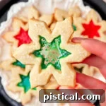 Crystal Window Bites 8 hand holding stained glass cookie over a plate of more cookies. centers are green and red.