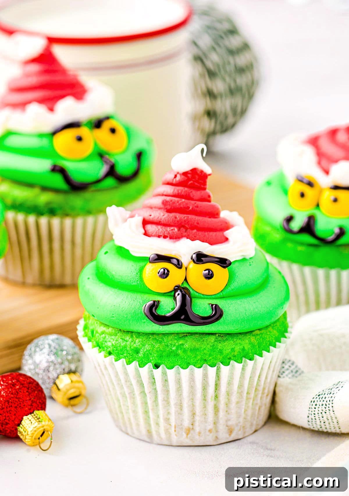 A festive Christmas cupcake decorated to look like the Grinch, complete with his green face and a vibrant red Santa hat, ready for holiday enjoyment.