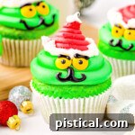 grinch cupcakes decorated with bright green frosting and a red santa hat in white cupcake liners.
