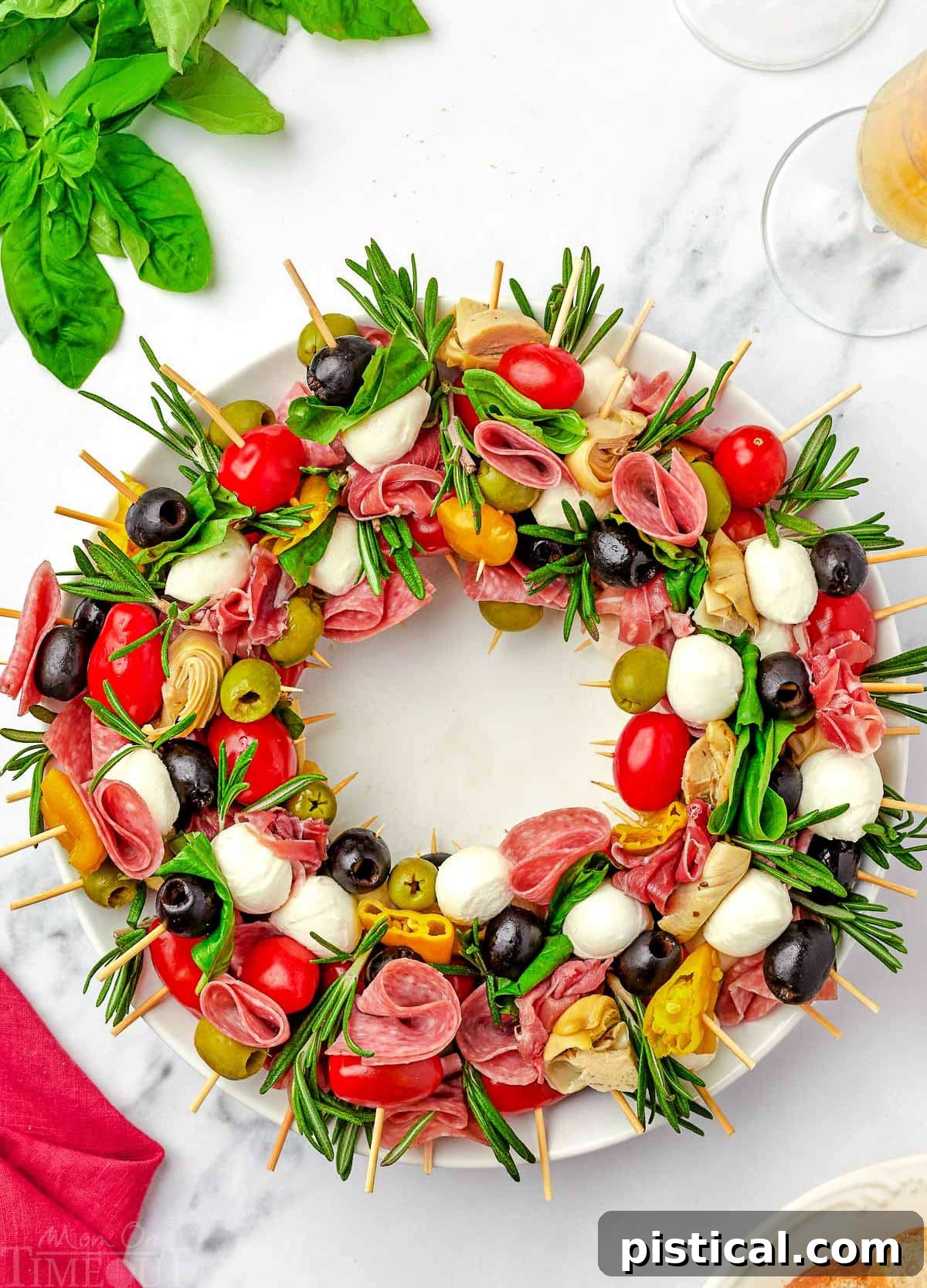 top down view of antipasto charcuterie wreath on a round white plate garnished with rosemary and basil.
