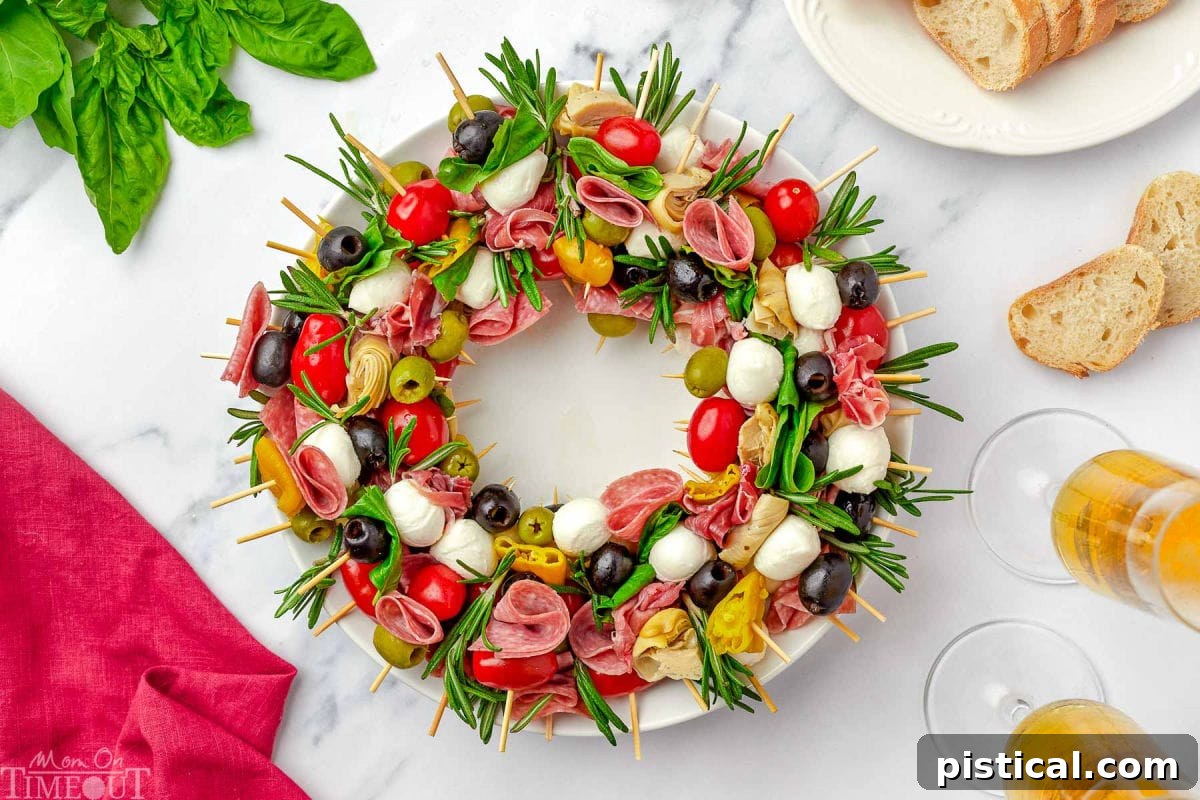 top down view of antipasto charcuterie wreath on a round white plate garnished with rosemary and basil.