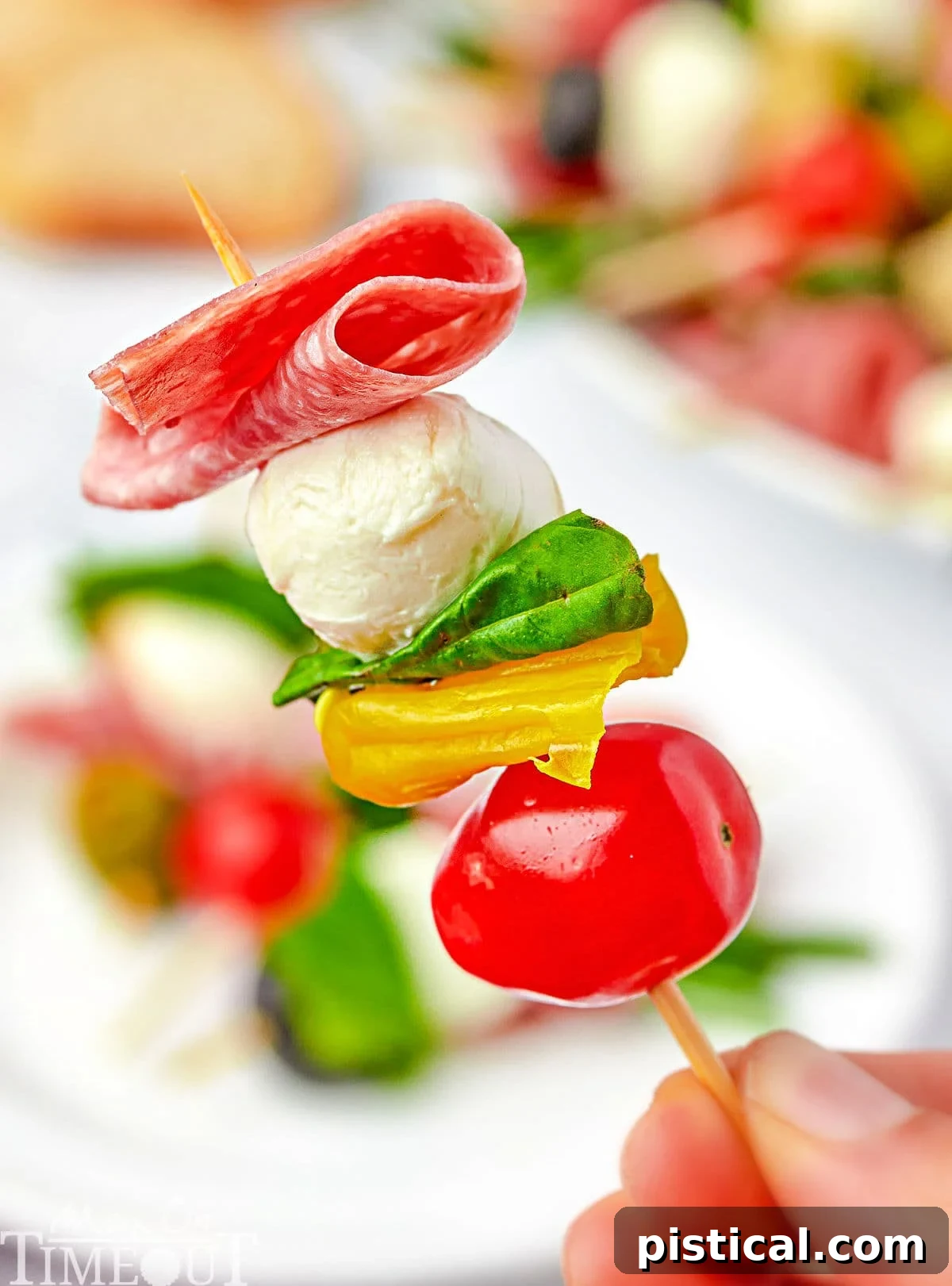 one antipasto skewer being held up over a plate.