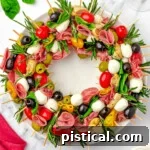 top down view of antipasto charcuterie wreath on a round white plate garnished with rosemary and basil.