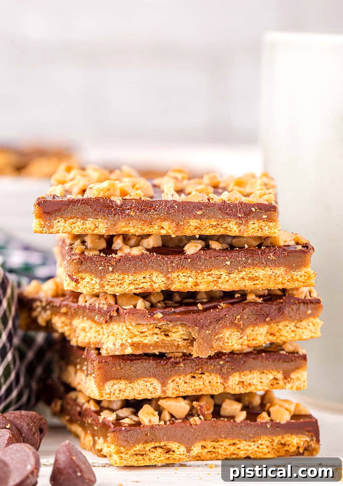 Six pieces of graham cracker toffee stacked on top of each other with some chocolate chips scattered in front, highlighting its sweet and crunchy appeal.