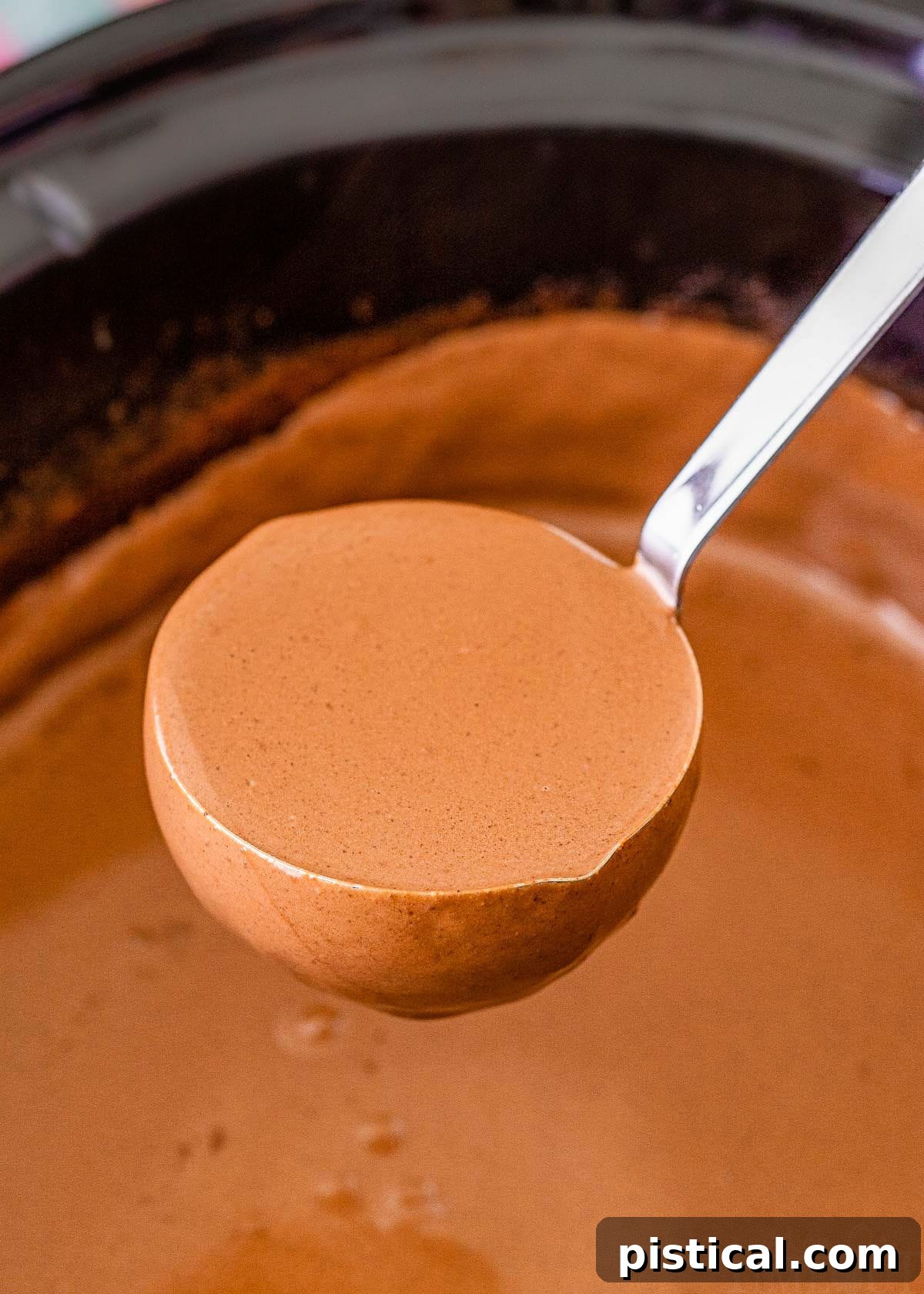 A ladle scooping out rich hot chocolate from a slow cooker, highlighting its creamy texture.