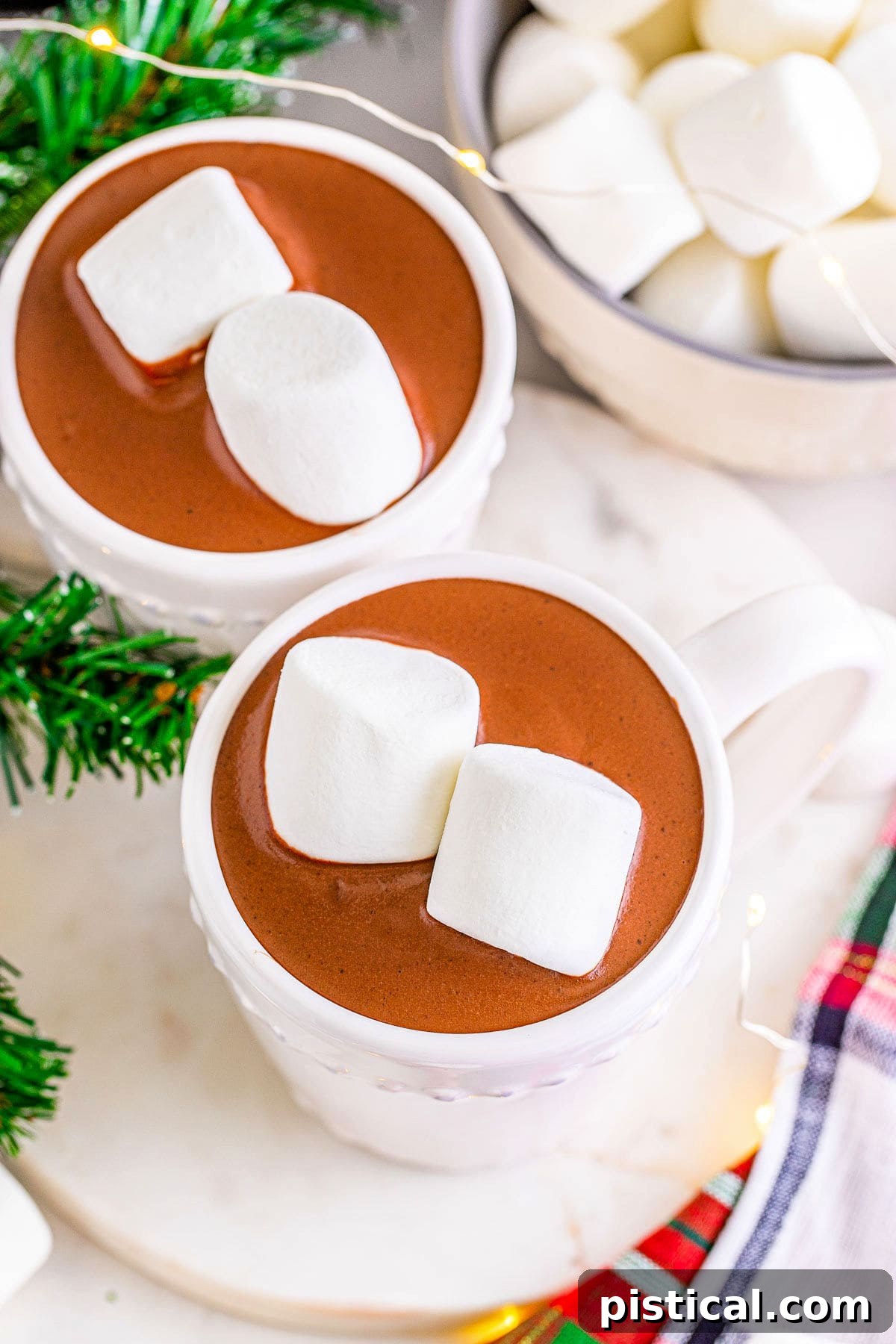 A top-down shot of two mugs of hot chocolate and a bowl of jumbo marshmallows, ready to be enjoyed.