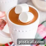 A white mug filled with decadent crockpot hot chocolate, topped with two jumbo marshmallows.