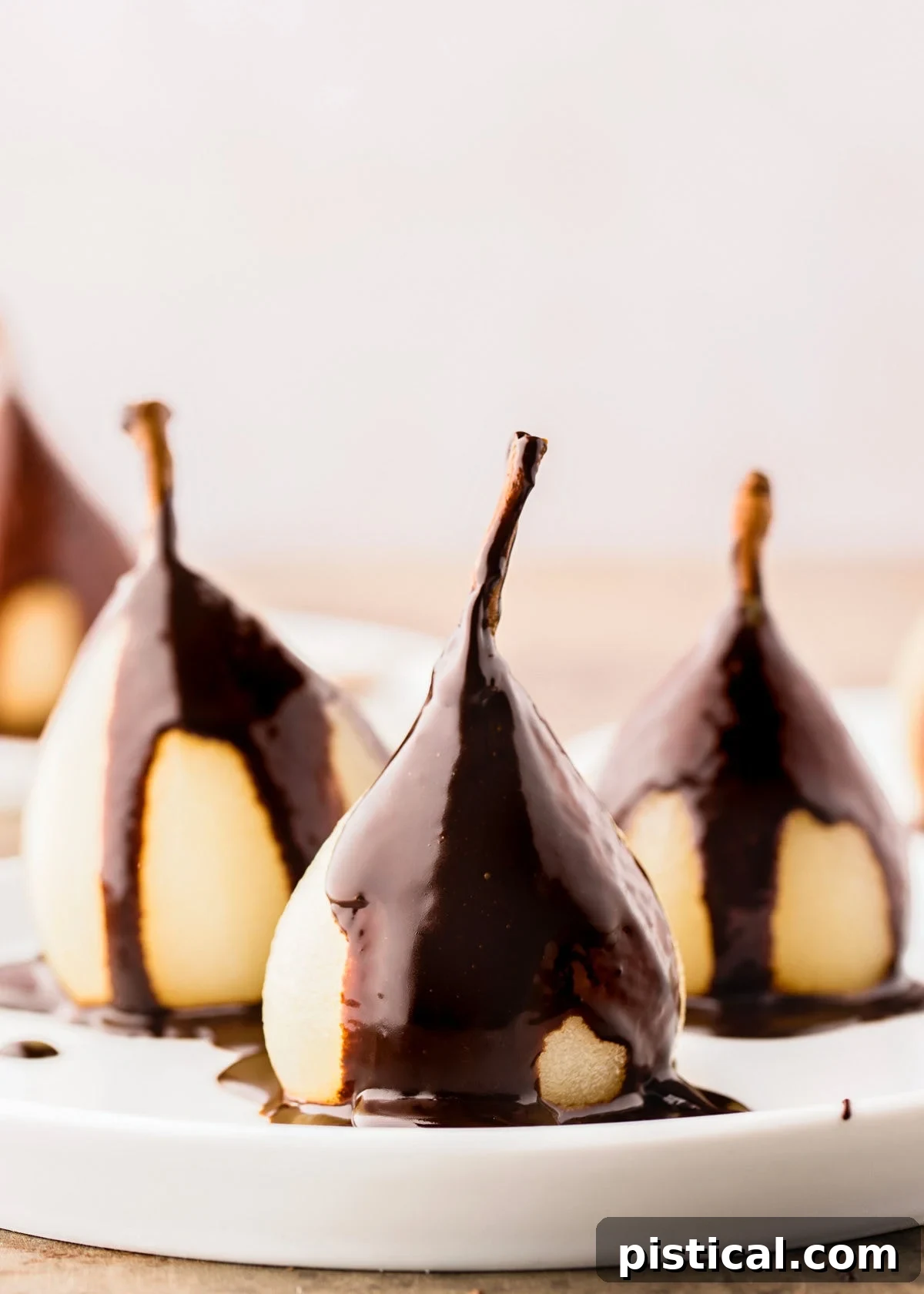 Velvet Pear Indulgence 3 three poached pears on a white plate topped with a creamy chocolate sauce.