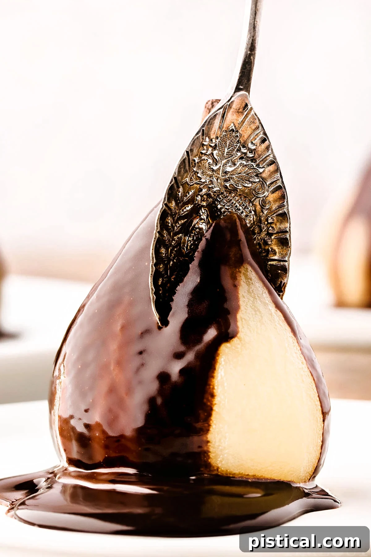 Velvet Pear Indulgence 9 poached pear on white plate topped with chocolate sauce and a vintage spoon is cutting into the pear from the top.