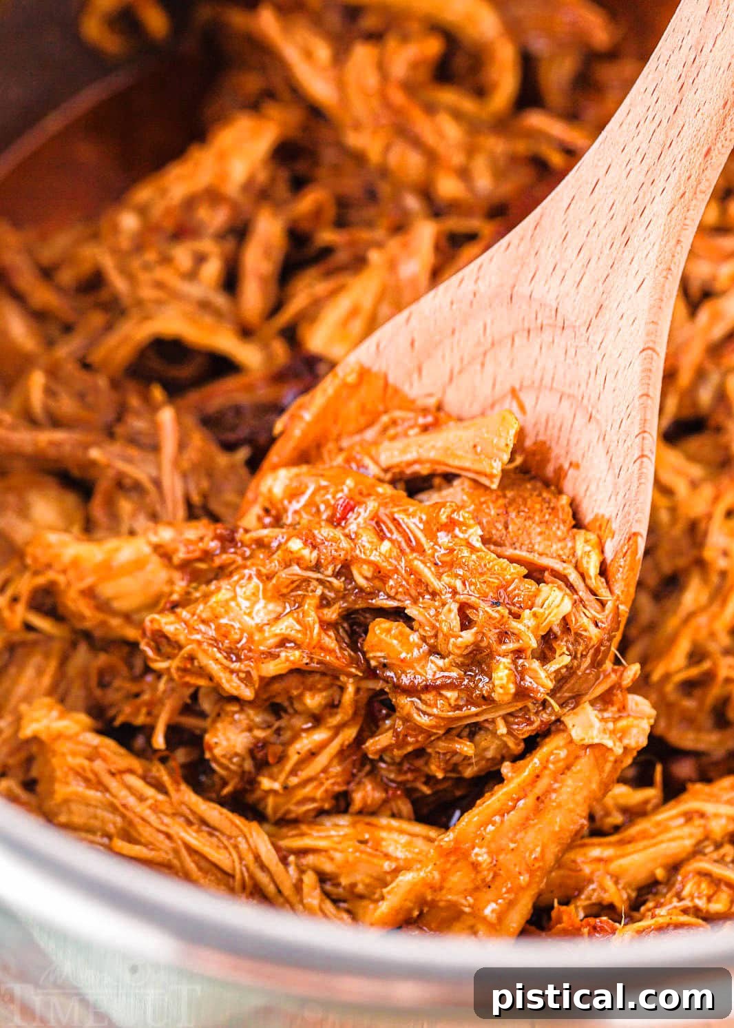Shredded pulled pork captured in an Instant Pot, with a wooden spoon showing its tender texture, ready for serving.