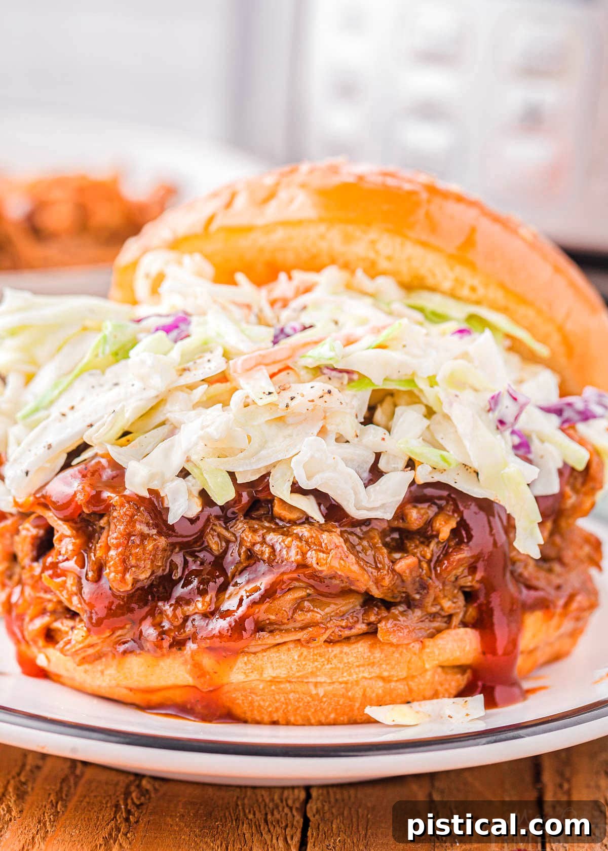 A beautifully assembled pulled pork sandwich, generously topped with creamy coleslaw, served on a white plate with an Instant Pot softly blurred in the background.