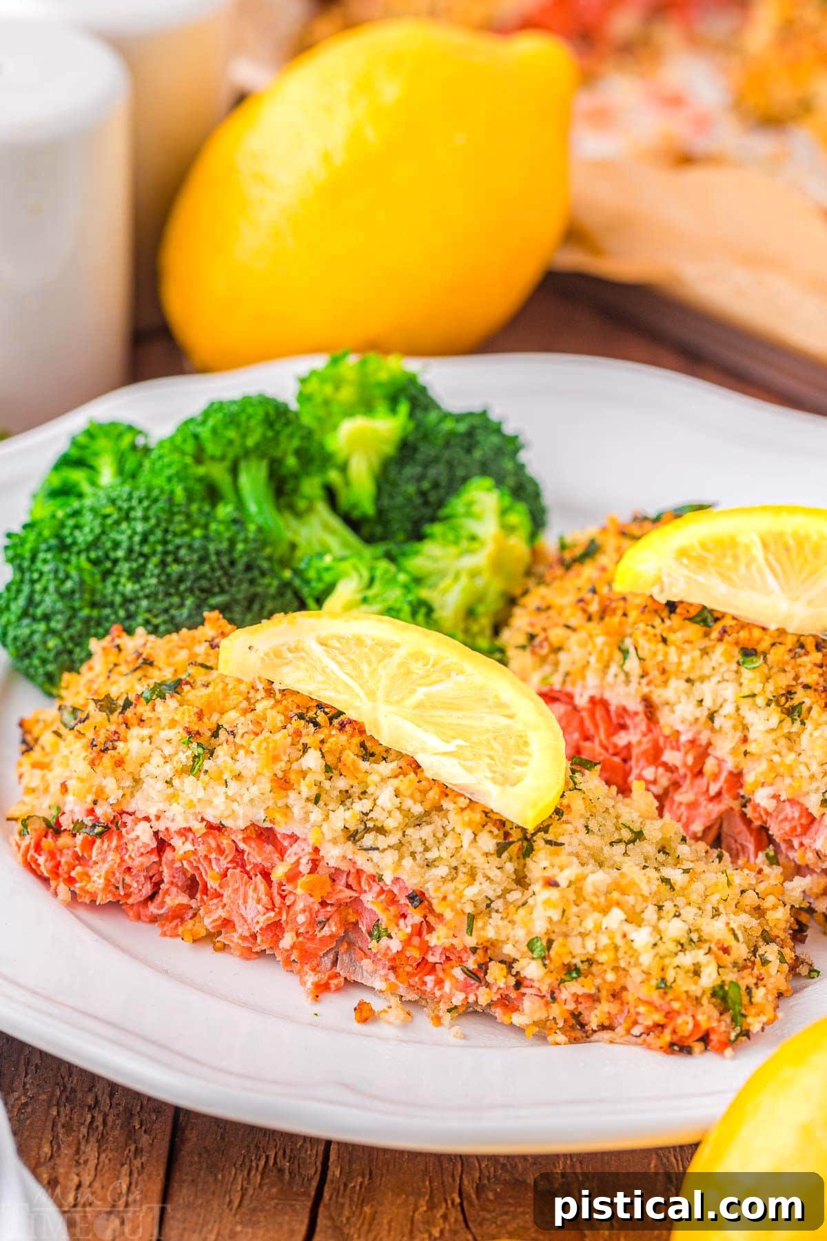 Crispy Parmesan Herb Salmon Bake 4 Two generous pieces of baked salmon, topped with a golden Panko and herb crust, served alongside steamed broccoli florets and a lemon slice on each fillet, arranged on a pristine white plate.