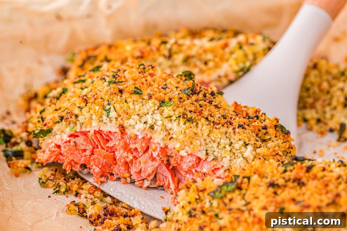 Crispy Parmesan Herb Salmon Bake 6 A perfectly baked piece of salmon with a golden-brown Panko crust being carefully lifted off a parchment-lined baking sheet using a spatula.