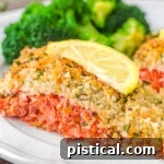 Crispy Parmesan Herb Salmon Bake 8 piece of salmon with a panko crust sitting on a plate with broccoli and a slice of lemon on top of it.