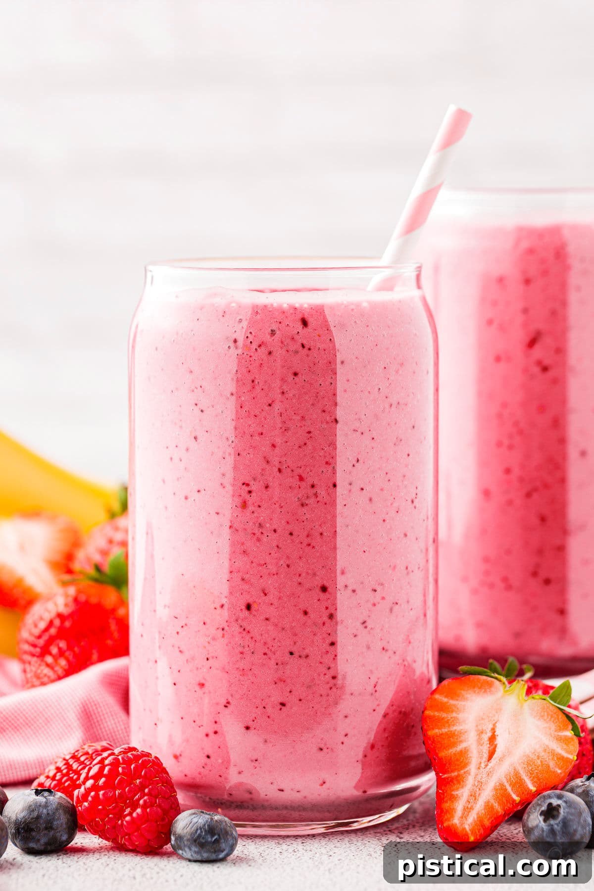 Two glasses of vibrant pink strawberry banana smoothies, artfully arranged with scattered fresh berries around their bases, creating an inviting and colorful display.
