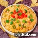 medium white bowl filled with rotel dip and topped with sliced green onions and diced tomatoes surrounded by blue and white corn tortilla chips.