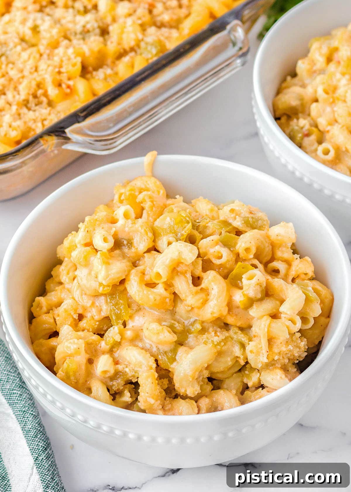 mac and cheese in a white bowl sitting on a marble surface. casserole dish and another bowl can be seen in the background.