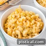 mac and cheese in a white bowl sitting on a marble surface. casserole dish and another bowl can be seen in the background.