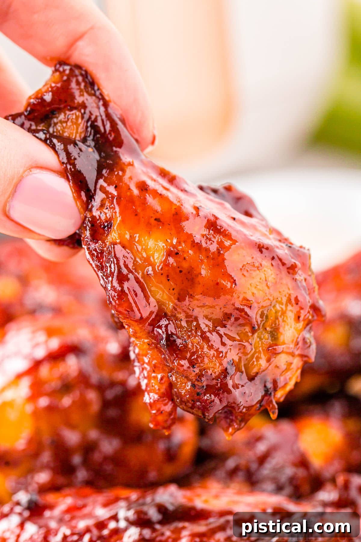 A hand holds a perfectly cooked BBQ Air Fryer Chicken Wing, showing its crispy texture and glistening sauce, ready to be devoured.