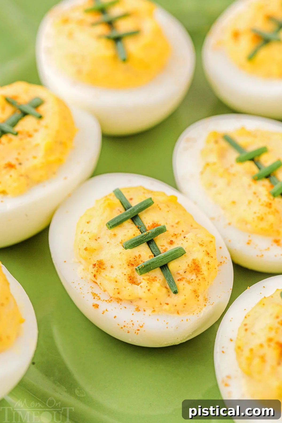 Touchdown Deviled Treats 2 Deviled eggs decorated with chives to resemble footballs, arranged neatly on a vibrant green plate.