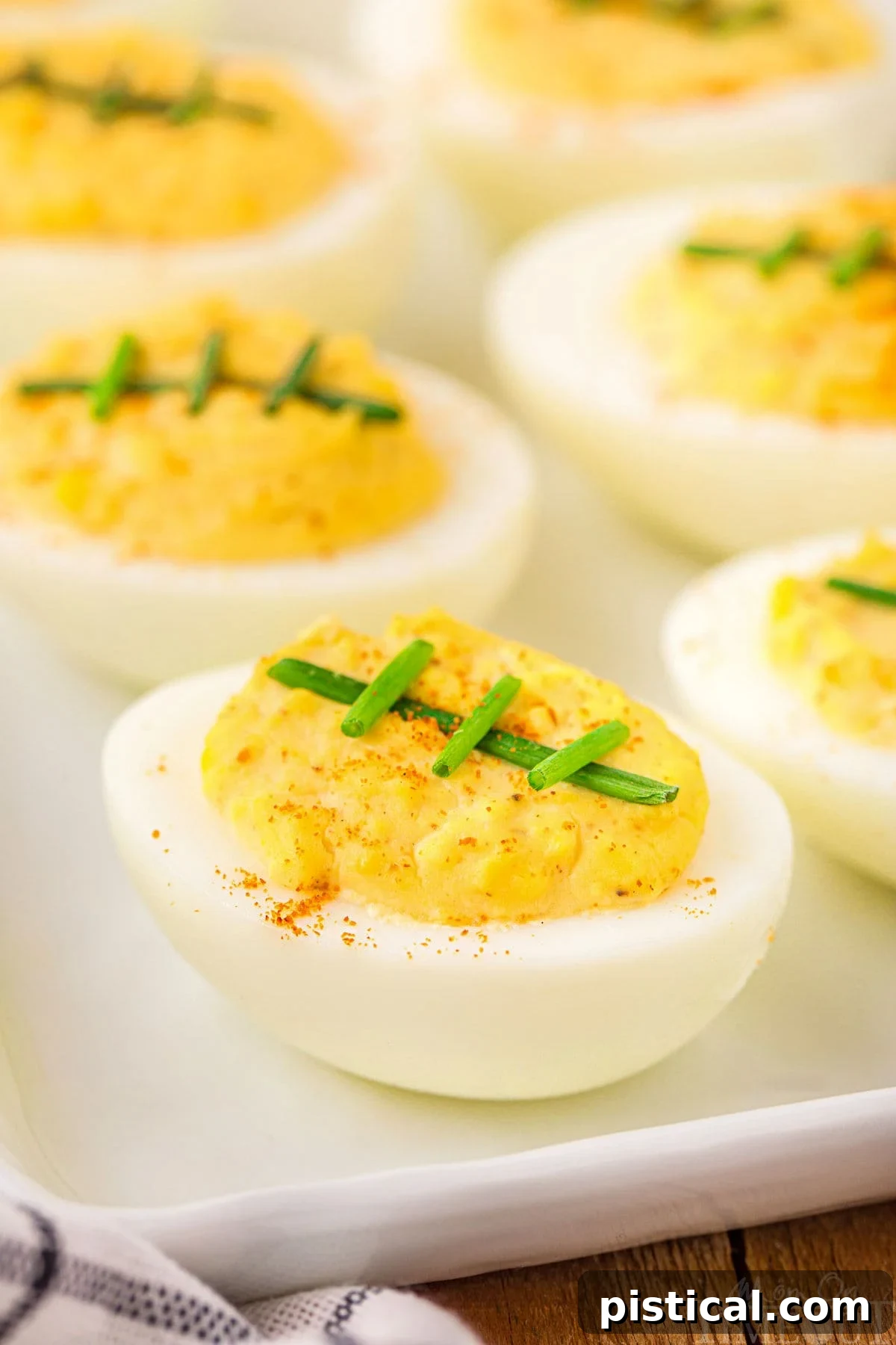 Touchdown Deviled Treats 3 A pristine white plate laden with football-themed deviled eggs, garnished with chives, ready for a spirited football party.