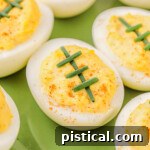 Touchdown Deviled Treats 7 deviled eggs decorated to look like footballs with chives on a green plate.