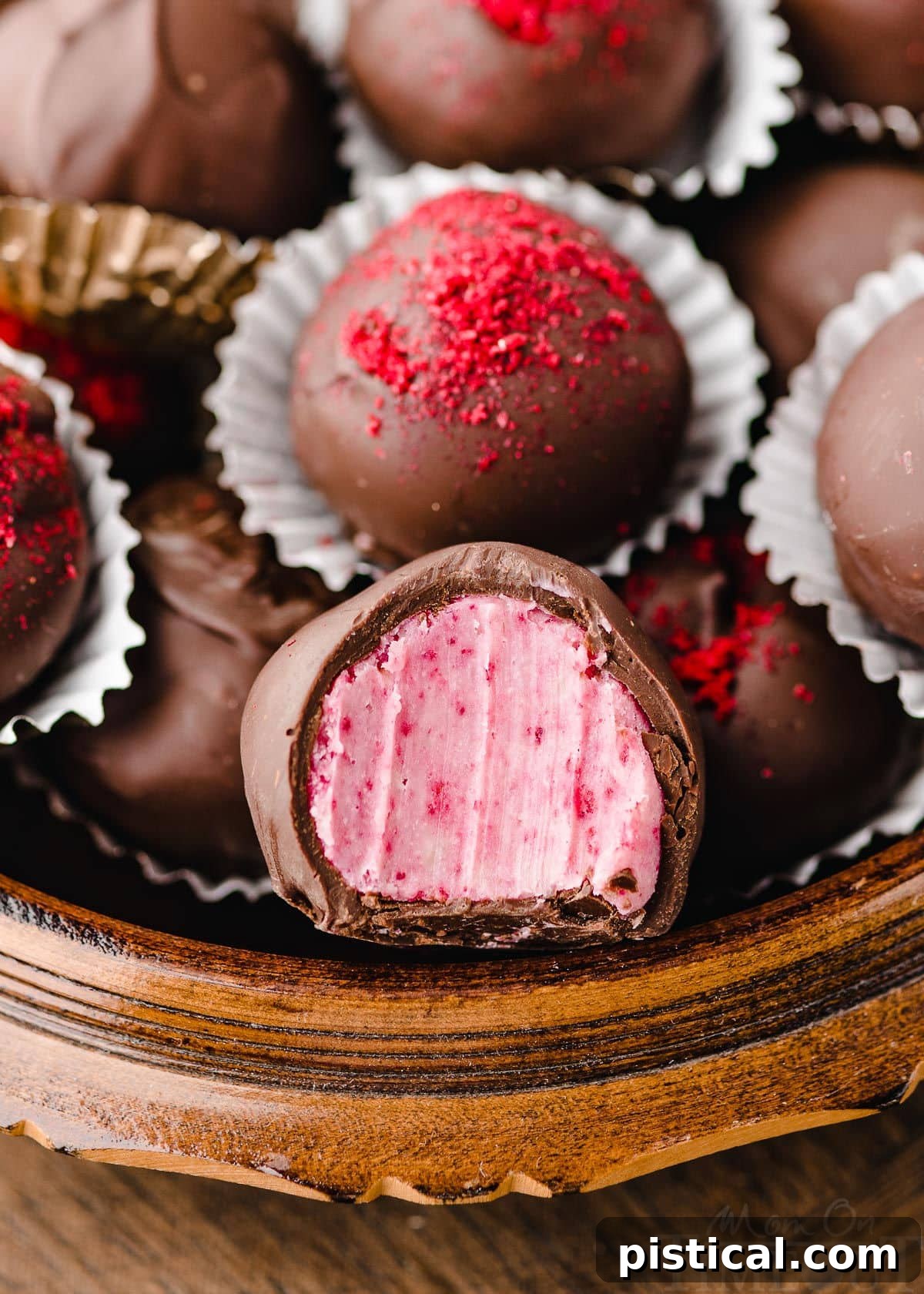 round wooden box filled with raspberry truffles. front truffle has a bite taken out of it. some of the truffles are topped with freeze dried raspberry dust.