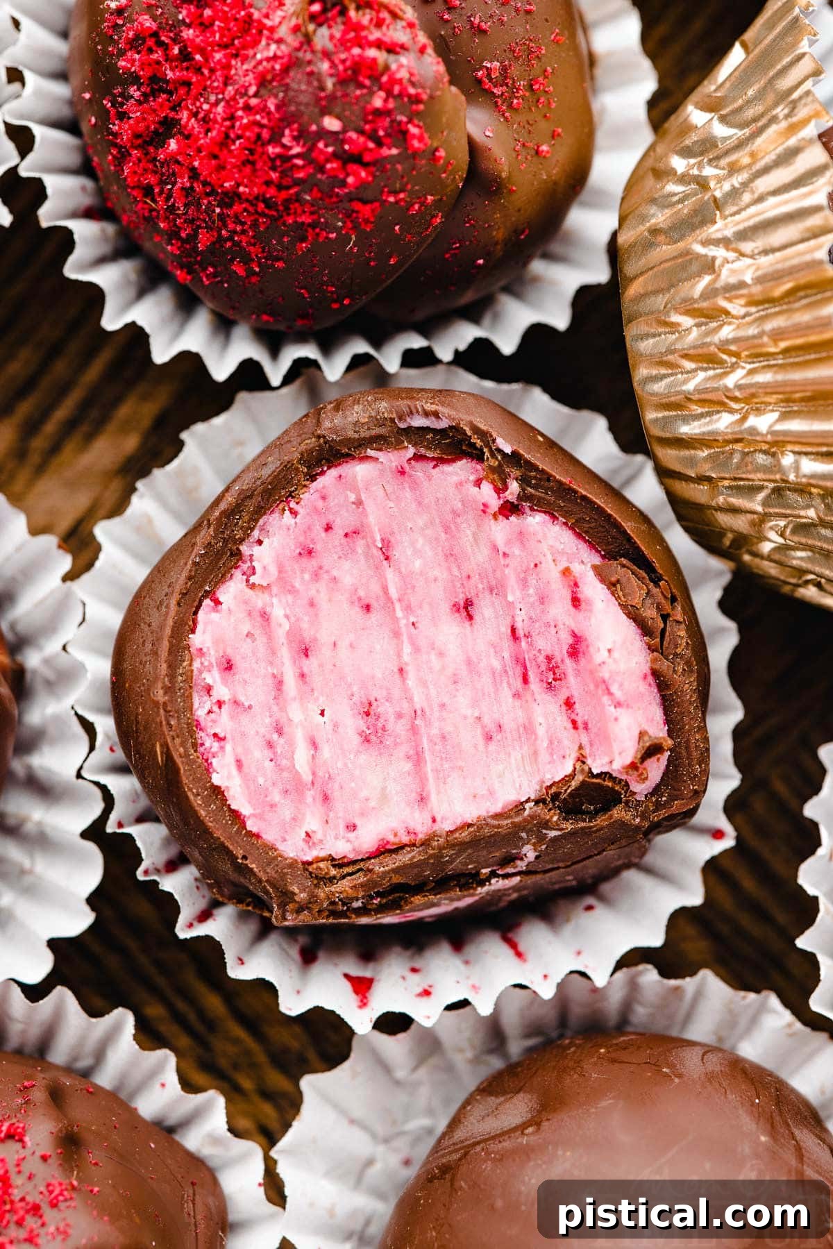 close up of a raspberry truffle covered in dark chocolate in small paper liners next to more truffles.