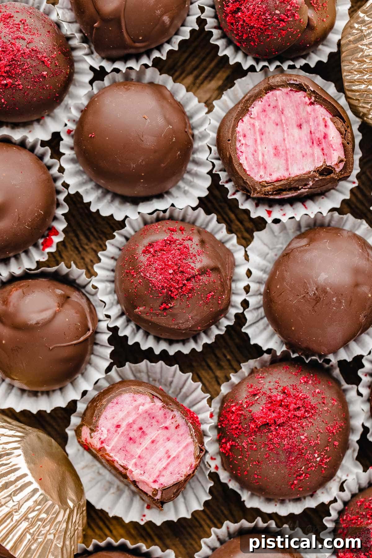 top down look at a dozen or so raspberry chocolate covered truffles in a wooden box. two of the truffles have been bitten in half.