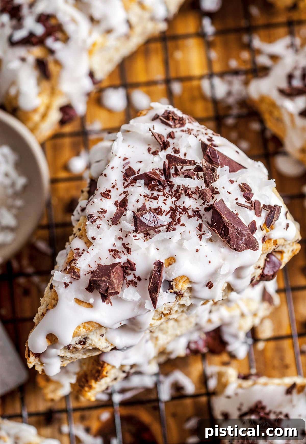 Three decadent Chocolate Coconut Scones, stacked and generously topped with creamy coconut icing and dark chocolate shavings, presented beautifully on a rustic wooden surface.