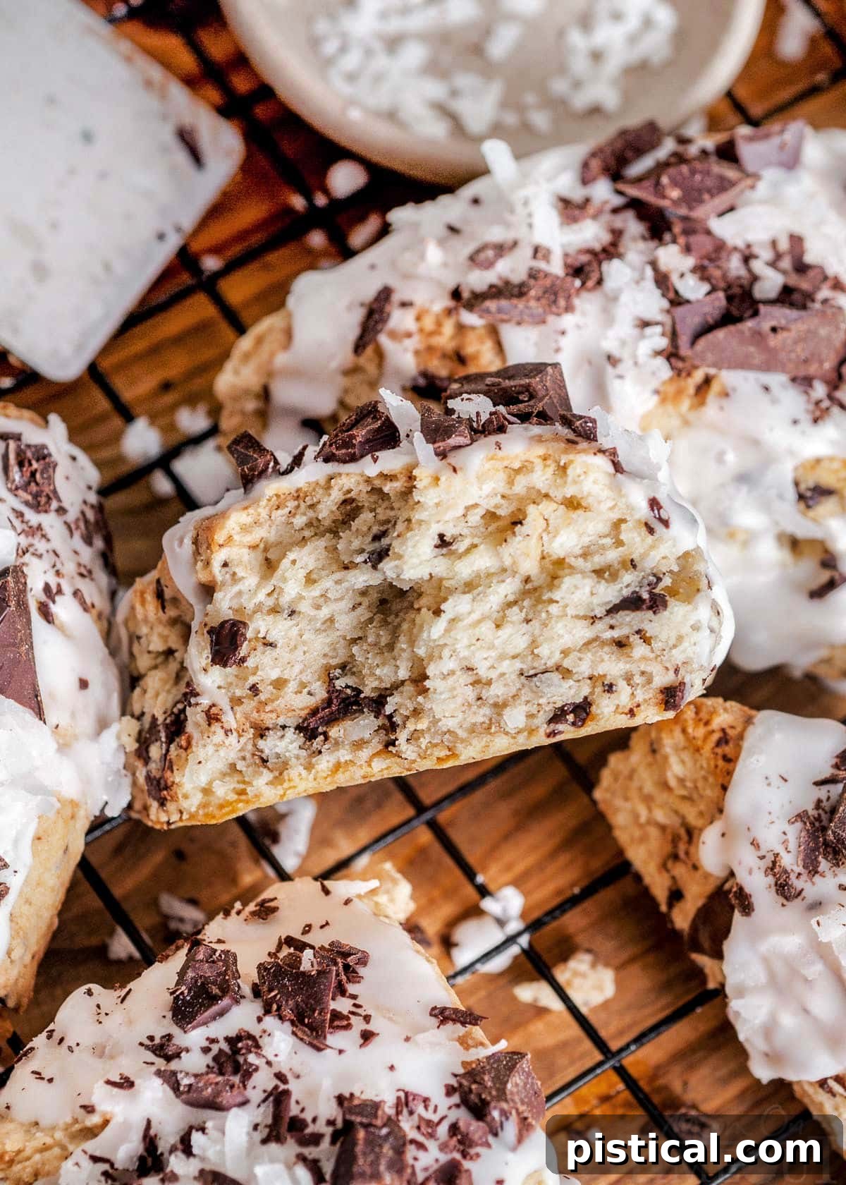 A freshly baked coconut scone, broken in half to reveal its tender, chocolate-studded interior, resting on a wire cooling rack beside other perfectly golden scones.
