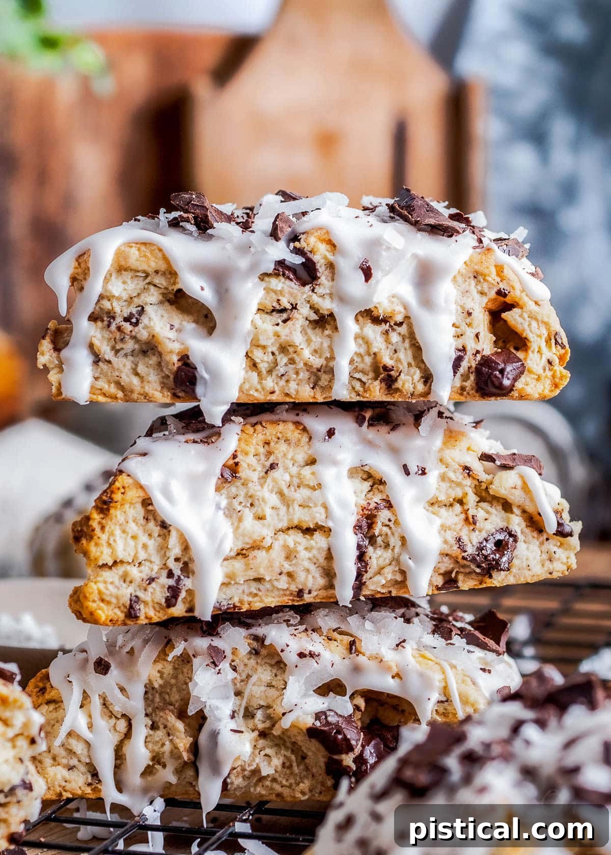 Three beautifully iced Chocolate Coconut Scones, stacked elegantly on a wooden board, ready to be served and enjoyed.