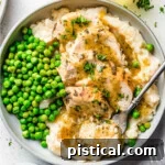 Easy Instant Pot Chicken Breast with Velvety Gravy 6 top down look at instant pot chicken breast sliced sitting on a bed of mashed potatoes with gravy over the top. green peas are also on the plate.