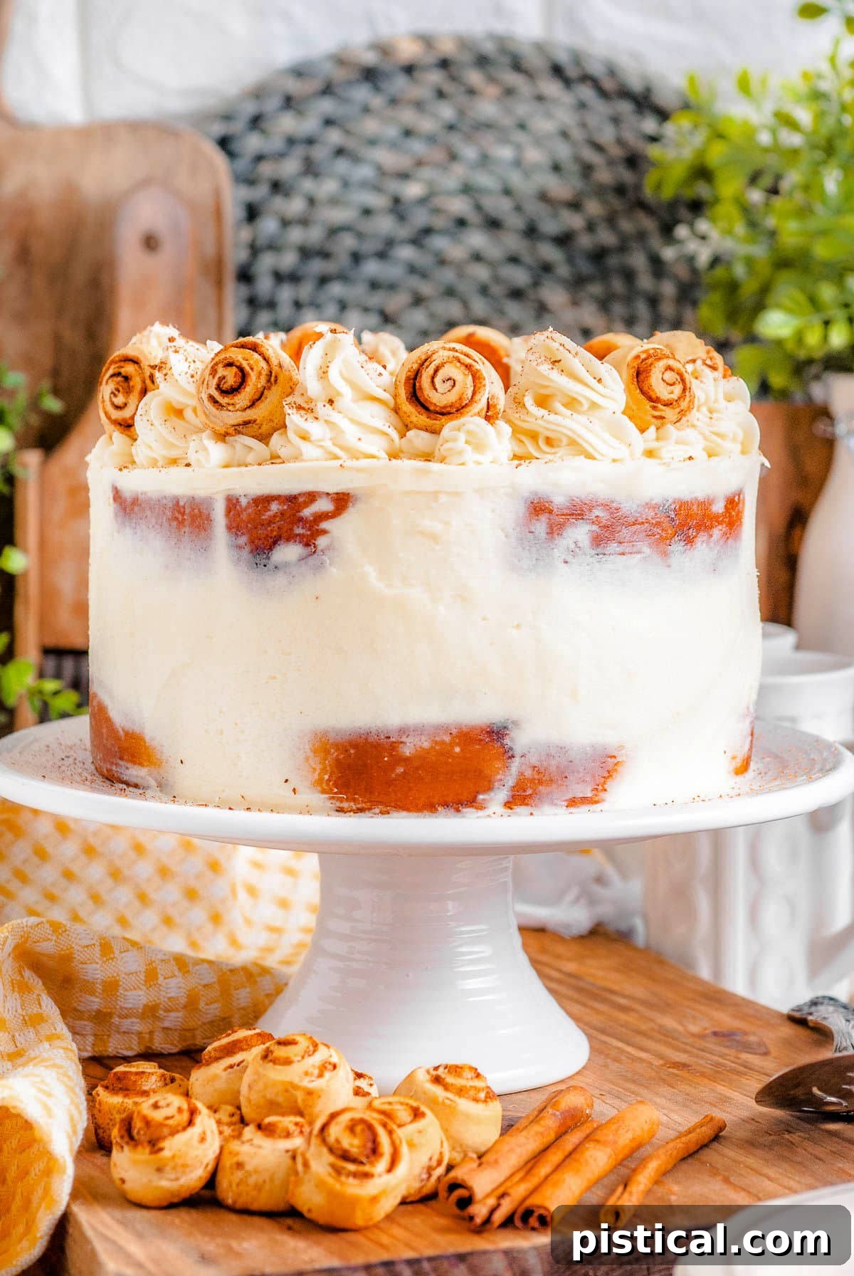 Decadent Cinnamon Swirl Layer Cake 11 A beautifully presented Cinnamon Roll Layer Cake on a white cake stand, adorned with cream cheese frosting and miniature cinnamon rolls, invitingly ready to be served.