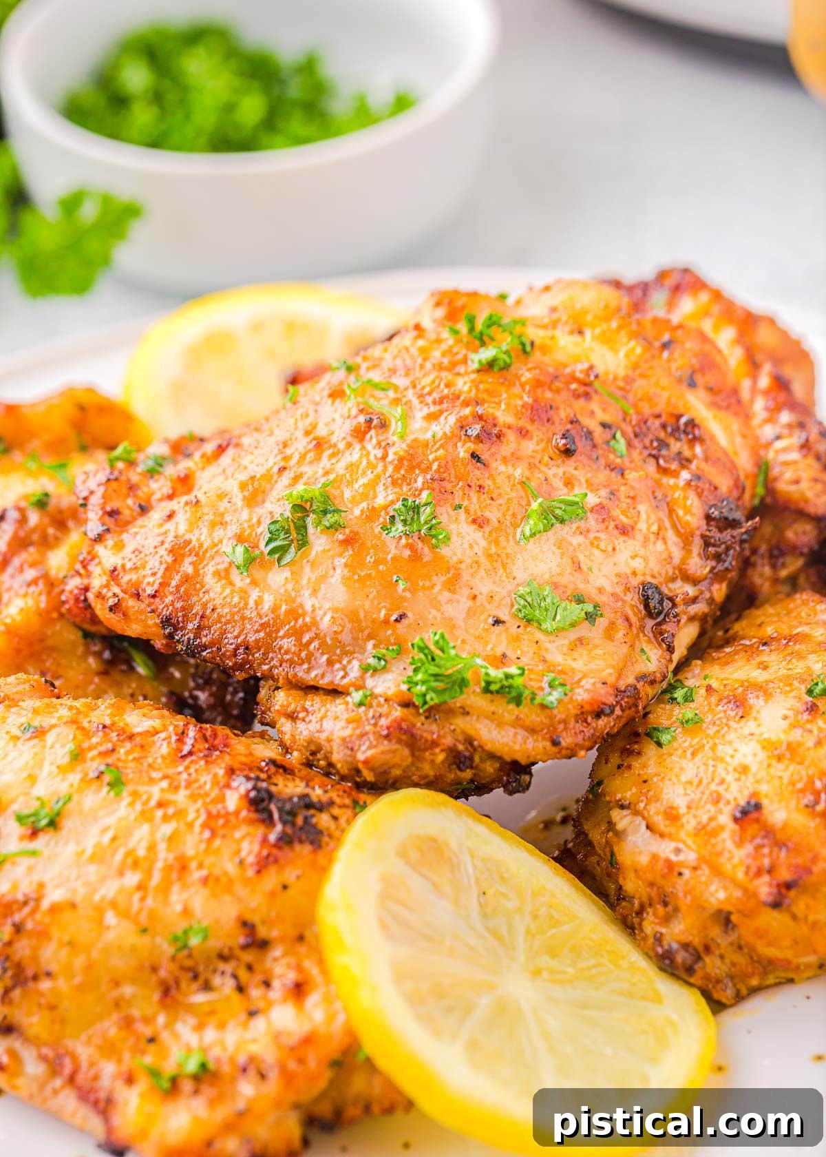 Four chicken thighs cooked in air fryer piled on a white plate and garnished with fresh parsley and lemon slices.