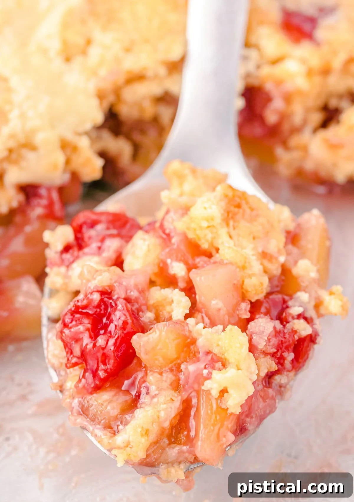 Tropical Cherry Pineapple Delight 6 A serving spoon filled with a scoop of cherry pineapple dump cake held over the baking dish.