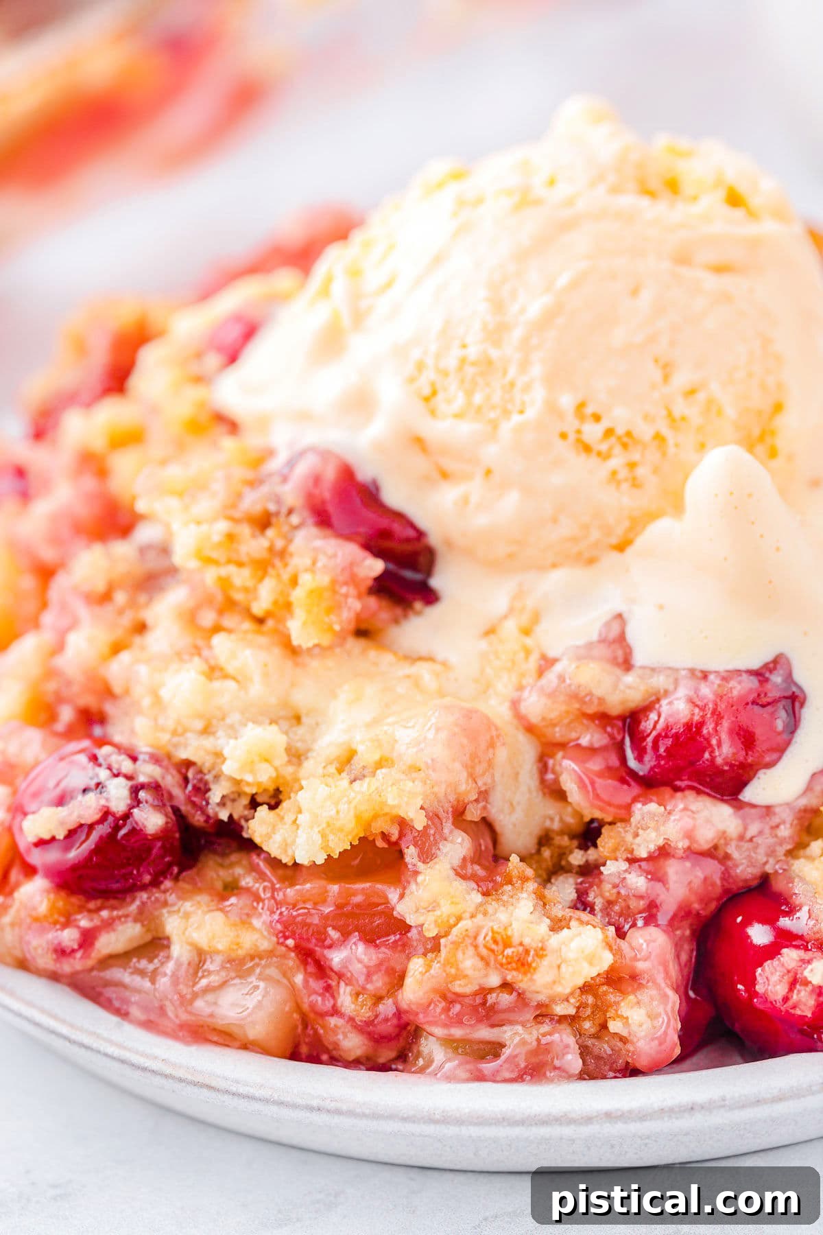 Tropical Cherry Pineapple Delight 7 A plate featuring a slice of cherry pineapple dump cake, adorned with a scoop of melting vanilla ice cream and visible fruit chunks.