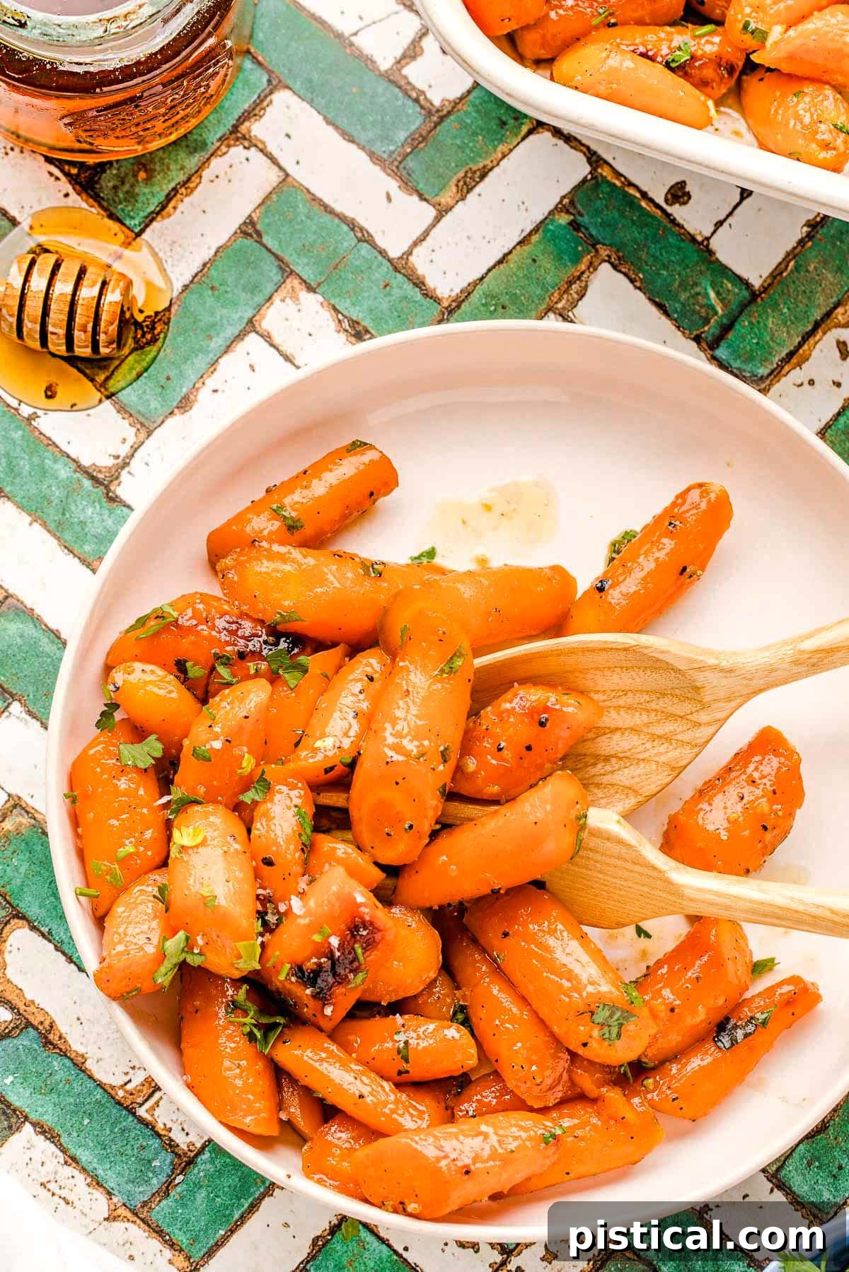 A plate of golden honey glazed carrots, garnished with fresh parsley, sitting on a modern teal and white tiled surface.