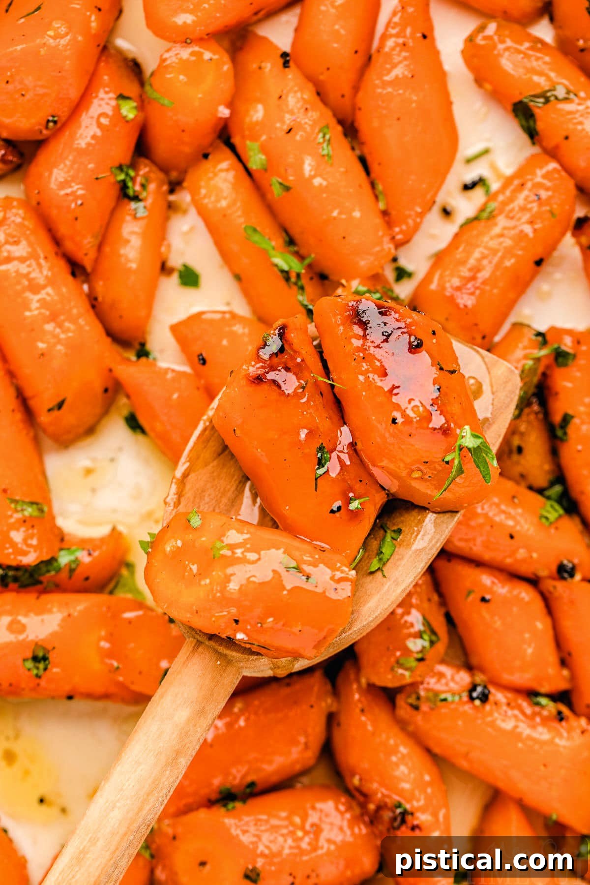 Honey glazed carrots on a baking sheet, featuring a wooden spoon holding three perfectly roasted carrots, ready to serve.