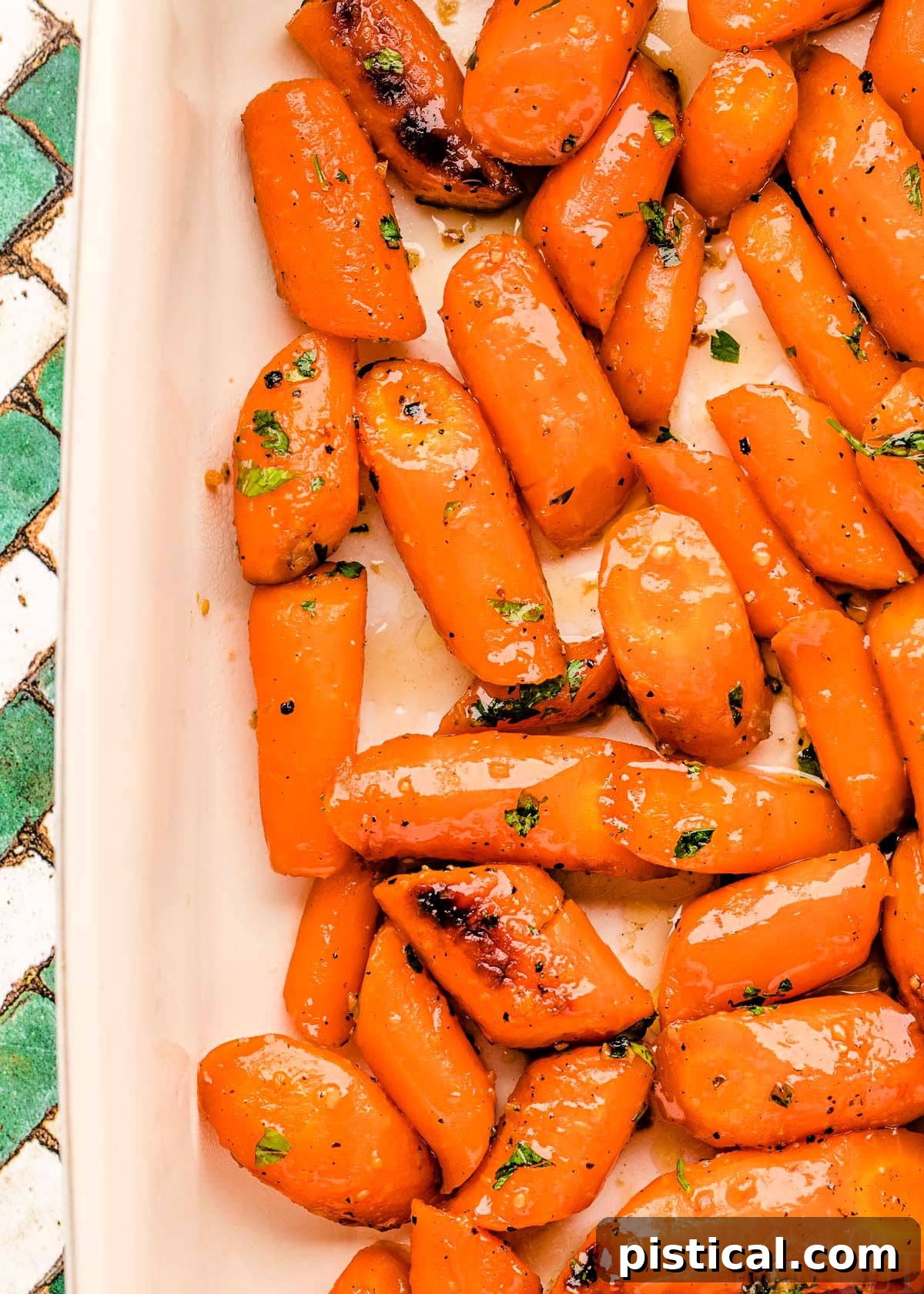 Close-up, top-down view of beautifully roasted honey glazed carrots, garnished with fresh herbs, in a white baking dish.