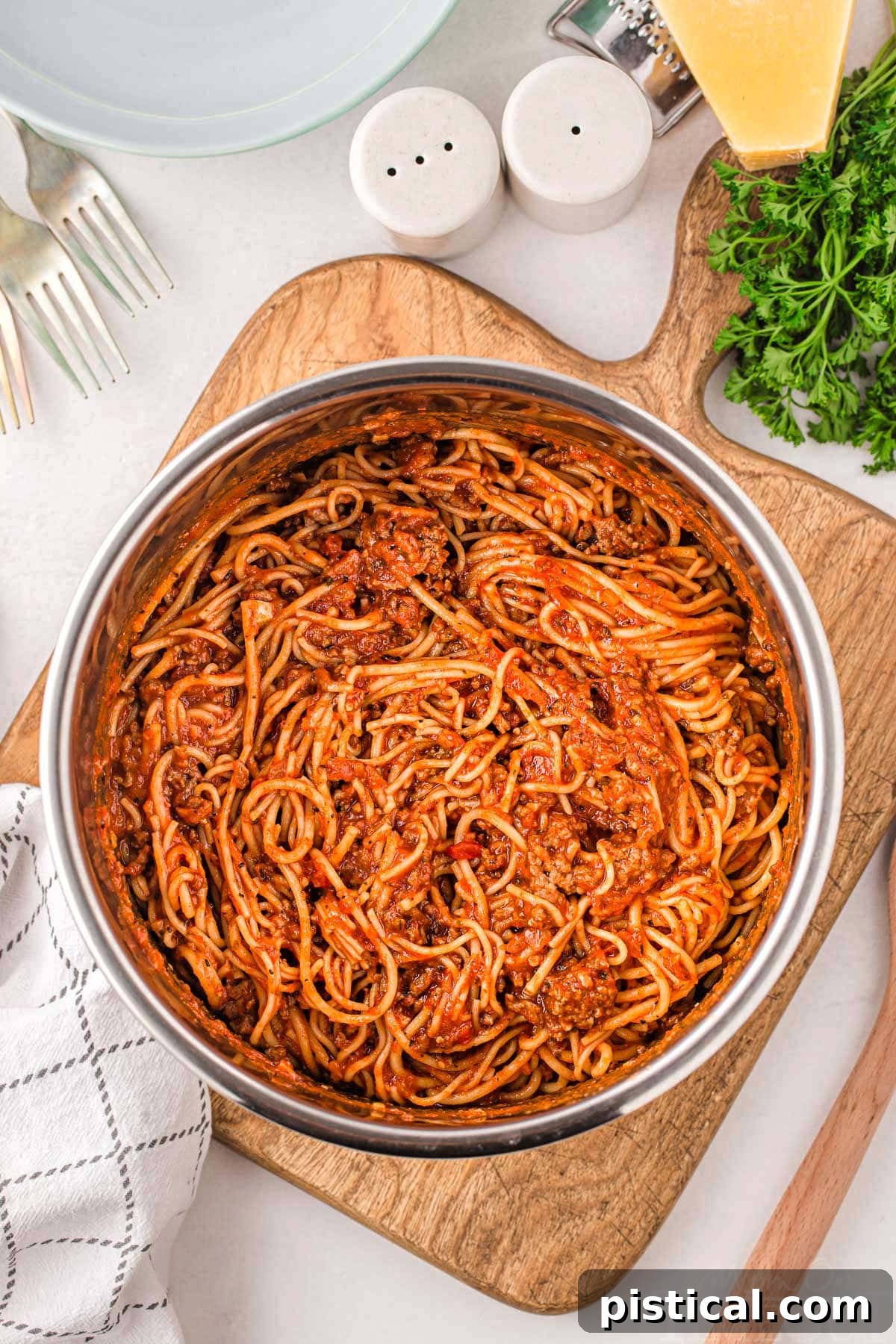Effortless Instant Pot Spaghetti 2 spaghetti in instant pot ready to be served sitting on a wood cutting board with parsley and parmesan next to the board.