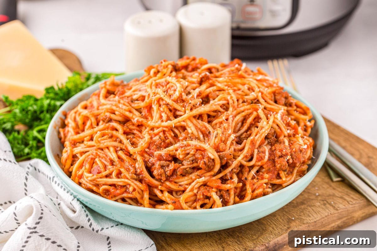 Effortless Instant Pot Spaghetti 4 aqua colored serving bowl filled with spaghetti sitting on a wood board next to a white towel in front of an instant pot.