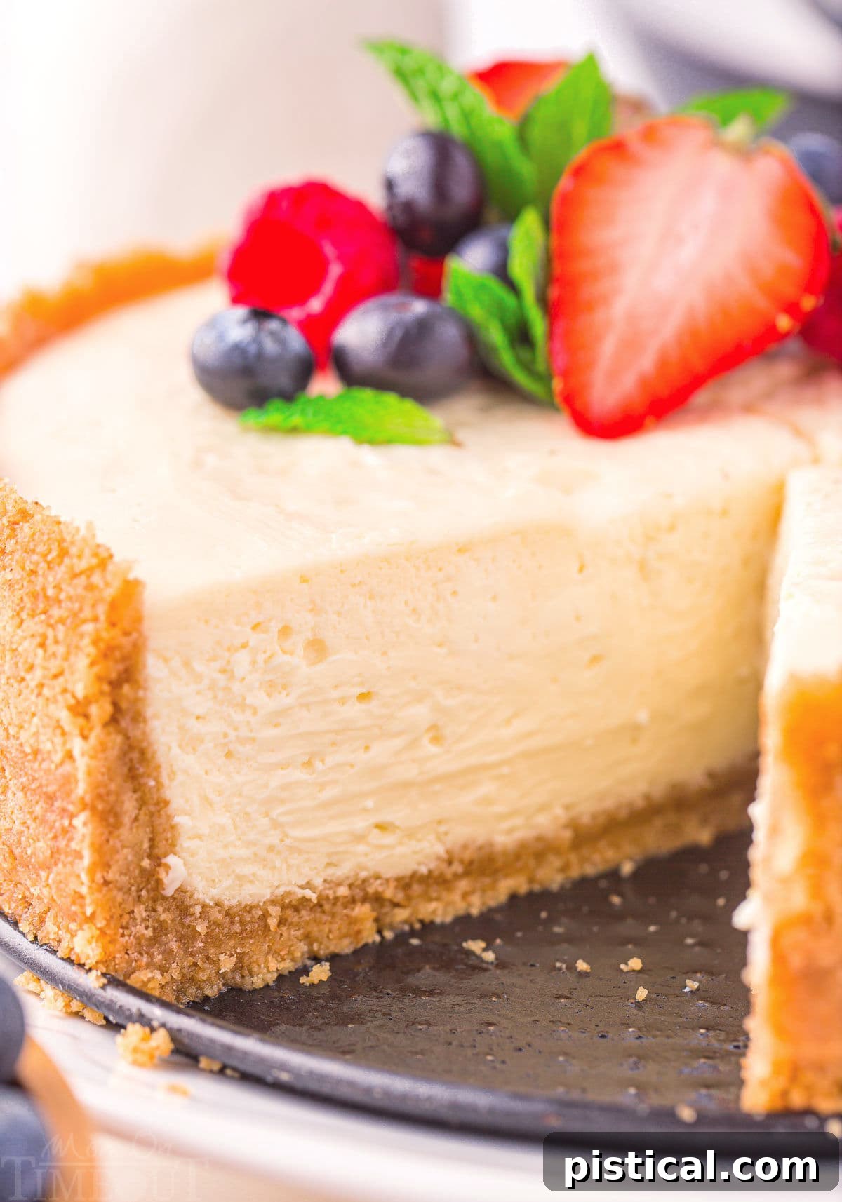 A close-up view of the interior of a perfectly cooked Instant Pot cheesecake, revealing its creamy texture. One slice has been removed, and the remaining cake is elegantly topped with fresh berries and a sprig of mint.