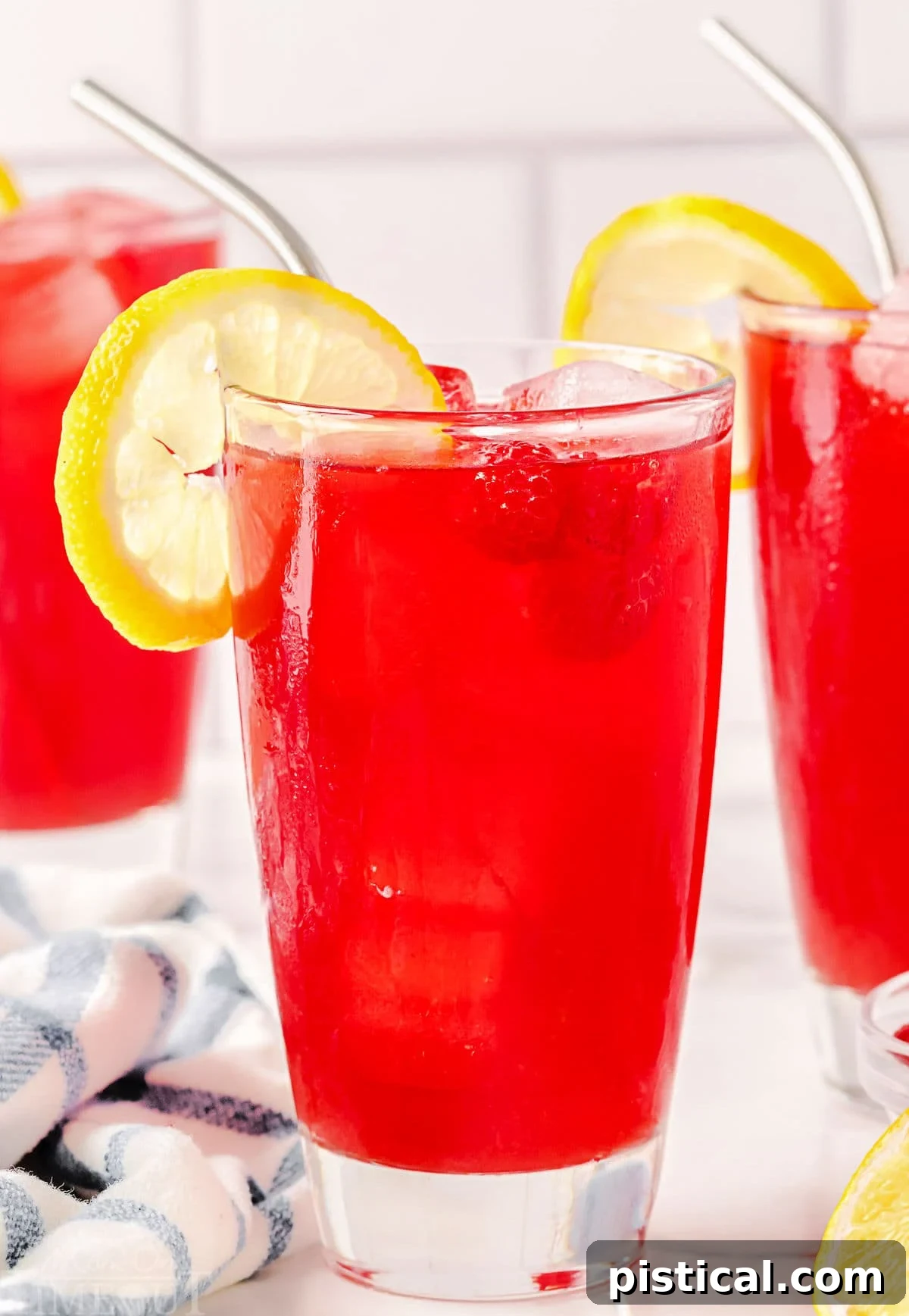 Ruby Red Raspberry Refresher 2 large tall glass filled with raspberry iced tea and topped with a lemon slice. two more glasses can be seen in the background.